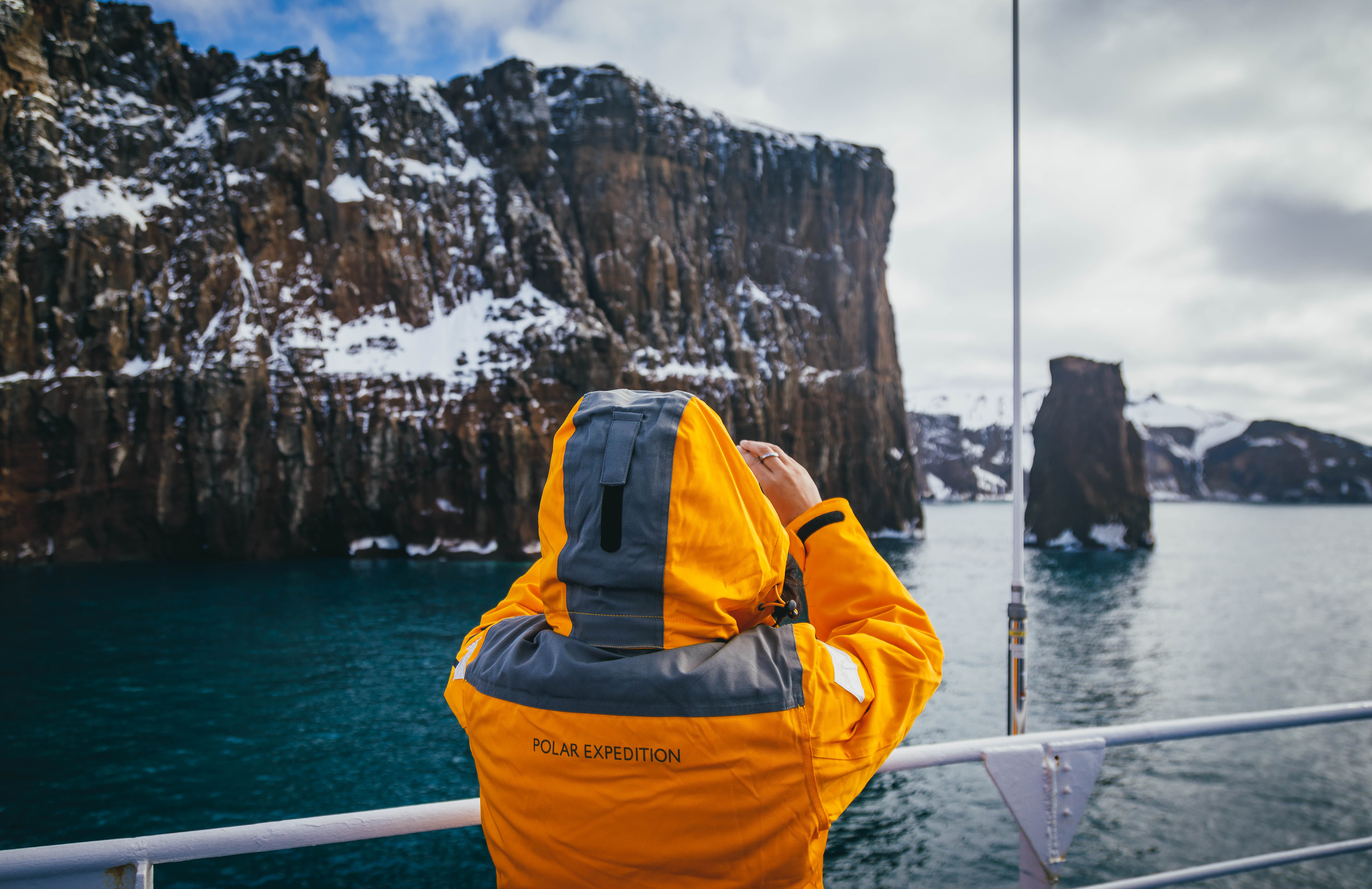 Guest in yellow parka stands on the main deck of their ship and takes a photograph with their smartphone