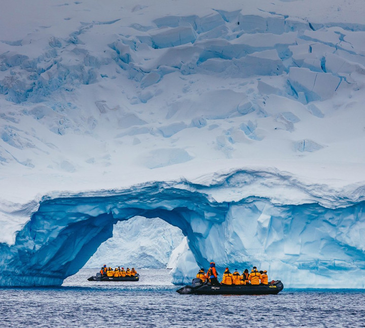 A zodiac boat is spotted through the arch of an iceberg near Cuverville Island. The zodiac boat appears to be close to the iceberg as a result of telephoto lens compression.