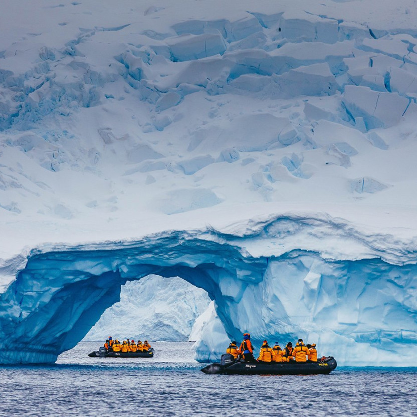 A zodiac boat is spotted through the arch of an iceberg near Cuverville Island. The zodiac boat appears to be close to the iceberg as a result of telephoto lens compression.