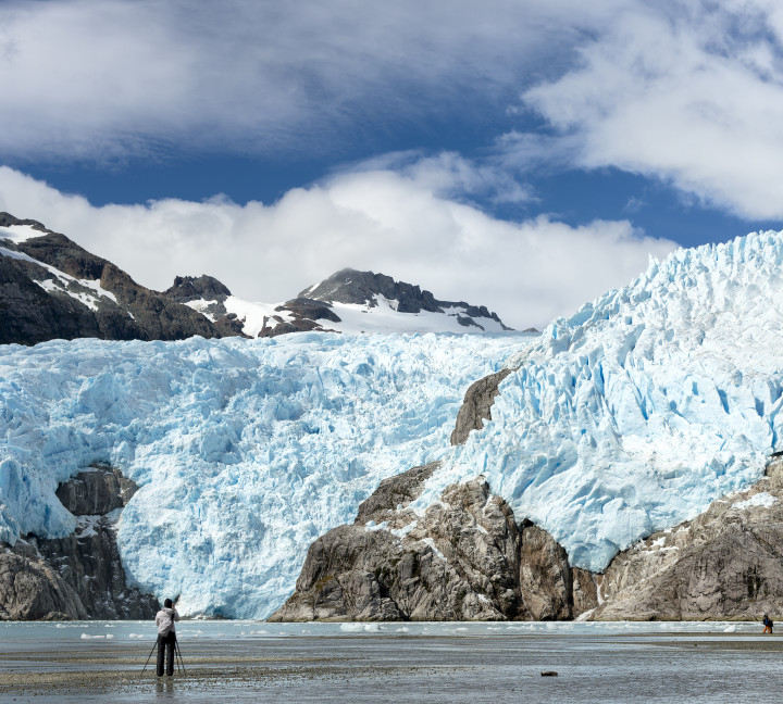 A photographer with a tripod stands in front of Capella Glacier at Santa Ines Island in the West Strait of Magellan.