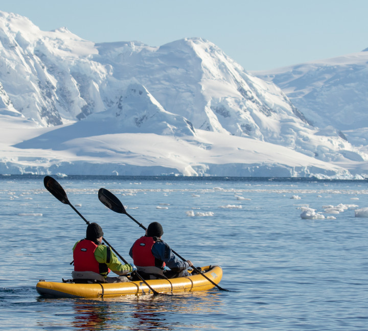 Two guests in dry suits paddle through Antarctic waters onboard our sit-on-top inflattable kayaks.
