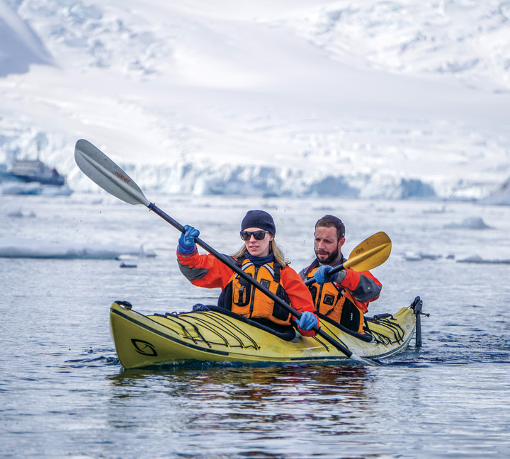 Two guests in their dry gear paddle a kayak in the frigid Antarctic waters during a sunny day.