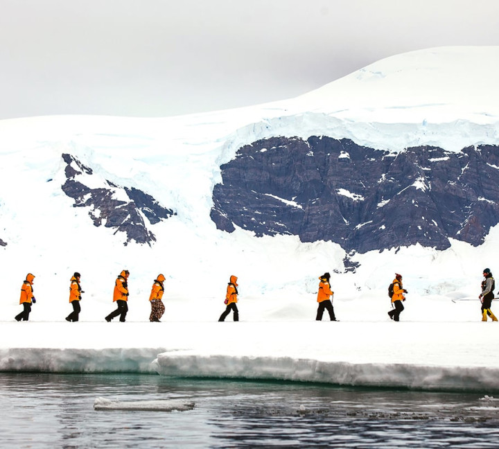 Guests in yellow parkas walk in a single file during a sea ice landing