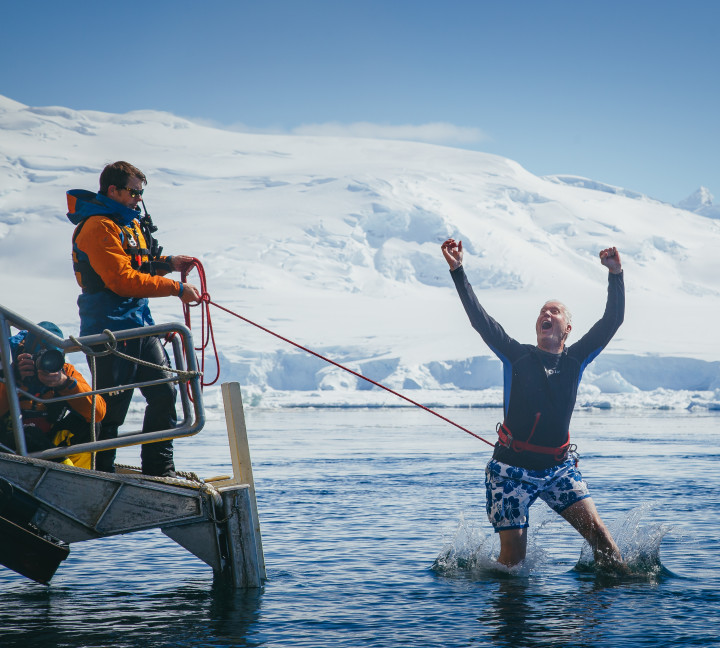 A guest secured with a harness jumps into Antarctic waters from a gangway/platform on their vessel.