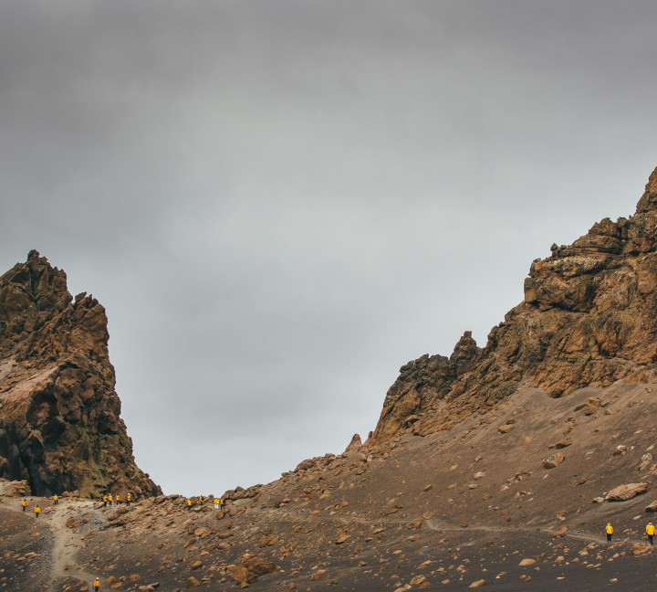 Guests in yellow parkas follow other guests up a hill at Deception Island, Antarctica.