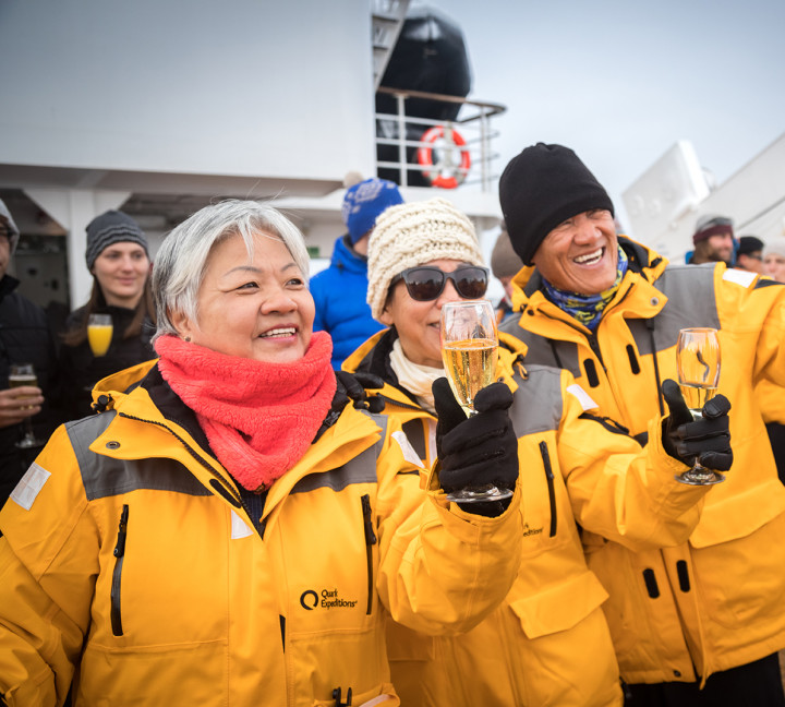 Guests celebrate crossing the Antarctic Circle with sparkling beverages and taking photos on the deck of the ship.