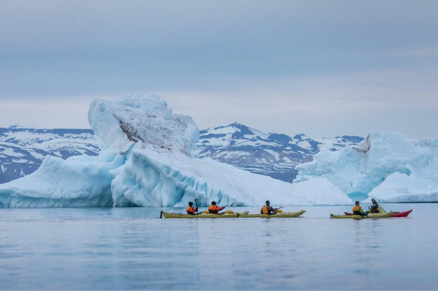 People kayaking near icebergs. 